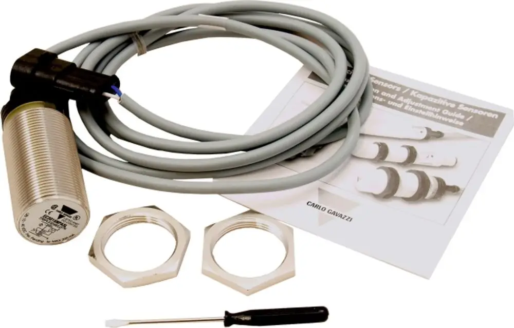 Proximity sensor mit grauem Kabel, darunter zwei Befestigungsmuttern und einer kleinen Schraubendreher. Enthalten ist eine Anleitung. Marke Wolf ist auf dem Sensor zu sehen.
